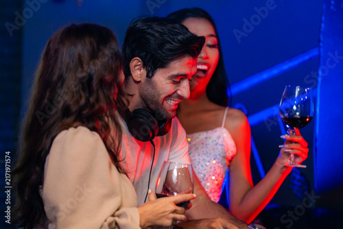 Photography A cheerful bearded DJ laughing shoulder to shoulder with two young female party guests laughs with his eyes shut while both guests hug him from the sides in a warm candid medium shot