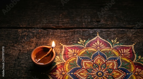 Beautiful Traditional Clay Oil Lamp Lit for Diwali Festival Celebration Over a Colorful Intricate Hand Drawn Mandala Pattern on Wood