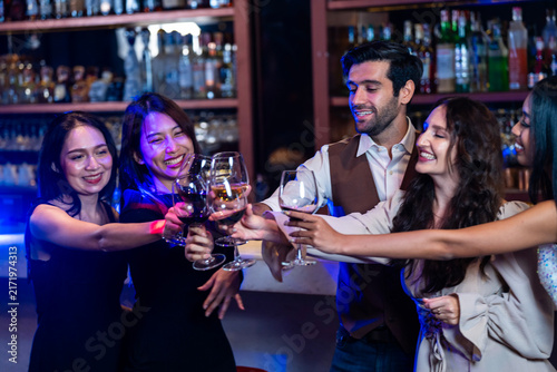 Sticker A cheerful male bartender toasting with a group of four young women at a crowded bar holds the toast while everyone smiles at the back bar of a modern nightclub