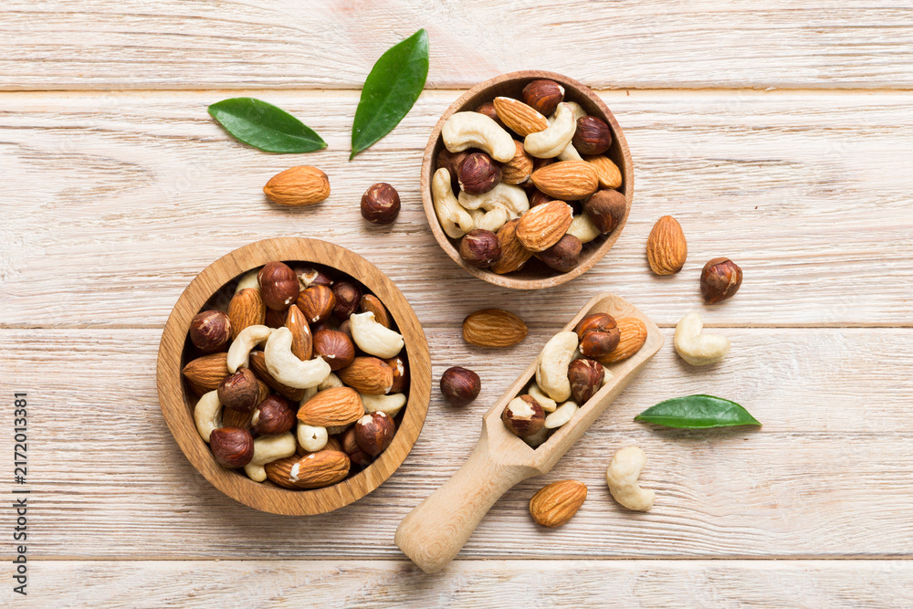 Fototapeta premium Assortment of nuts in wooden bowl on colored table. Cashew, hazelnuts, walnuts, almonds. Mix of nuts Top view with copy space