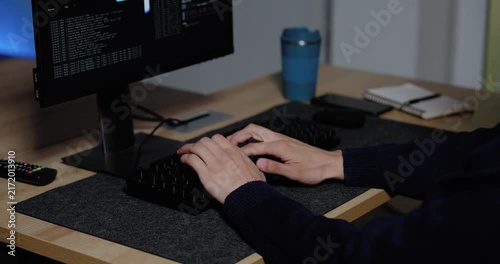 Technology professional typing source code on keyboard while multiple monitors display software interface in modern office, supporting programming workflow, system analysis, cybersecurity project.
