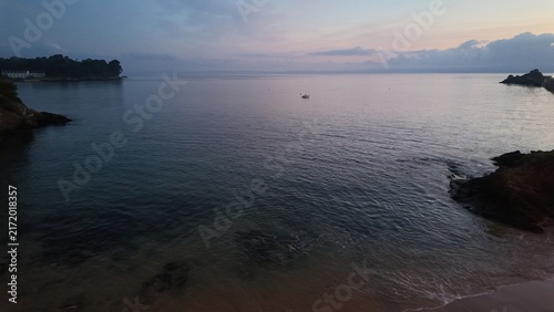 Bild auf Leinwand Lever de soleil serein sur l'océan calme en Bretagne, France, avec un petit bateau flottant paisiblement au milieu de la baignade et des côtes rocheuses