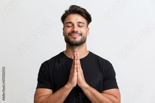 Young man with a beard stands with his hands pressed together in a peaceful prayer gesture