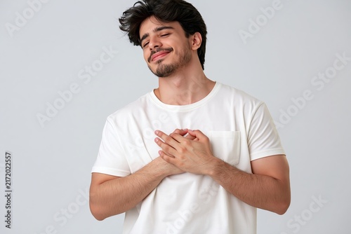 Young man with a peaceful expression holds his hands over his heart in a gesture of gratitude