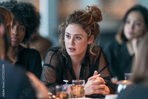 Young woman with curly hair speaking during a business meeting with colleagues in a cafe setting