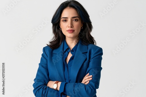 Confident young woman in a blue blazer stands with her arms crossed looking at the camera