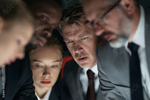 Diverse group of business people looking down at a glowing screen in a dark office environment