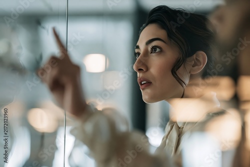 Focused young woman touching a glass screen in a modern office environment with soft lighting