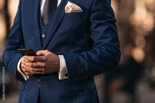 Man in a sharp blue suit using a smartphone while standing outdoors in a city environment