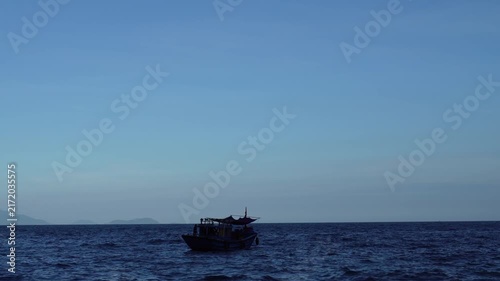 Small wooden fishing boat sailing on the open blue sea under a clear sky