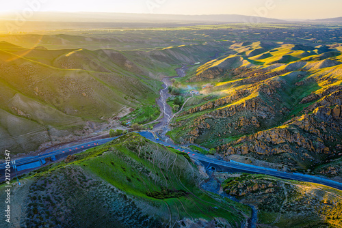Foto Scenic mountain landscape with a winding highway and rolling green hills illuminated by warm golden sunlight during sunset