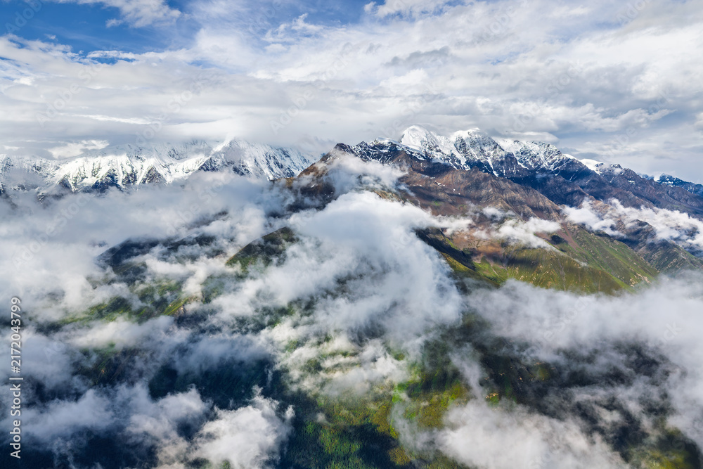 Obraz premium Breathtaking scenery of snow covered mountain range surrounded by clouds in Sichuan, China.