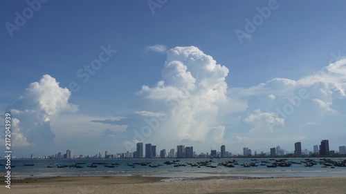 Coastal city skyline with fishing boats under massive white cumulus clouds