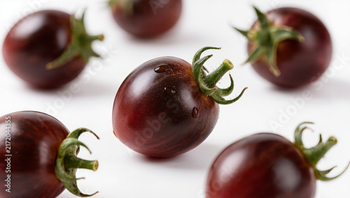 Dark purple cherry tomatoes with water drops on a white background, fresh organic heirloom vegetable and healthy food macro with copy space for text