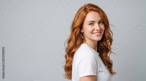 Smiling young woman with natural copper hair posing in studio against gray background