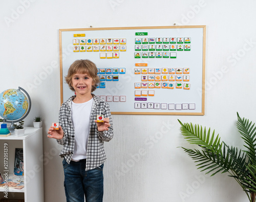 Foto Smiling schoolboy holds colorful picture word cards in front of a magnetic learning board while practicing English vocabulary, grammar and sentence building skills