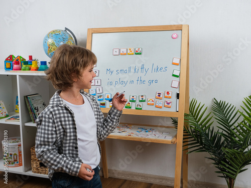 Bild auf Leinwand Schoolboy writes an English sentence on a learning board while using colorful word and picture cards as visual aids for practicing grammar, vocabulary and sentence building