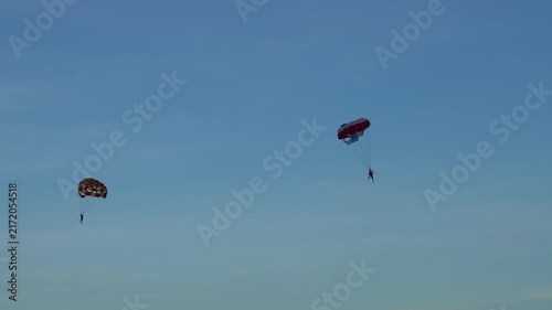 Two parasailers flying colorful parachutes in a clear blue sky