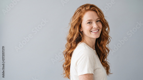 Smiling Young Woman with Long Curly Copper Hair Posing against Neutral Gray Studio Background