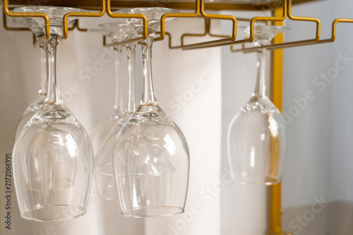 Принти на полотні Clear wine glasses hanging upside down on gold metal rack in modern kitchen or b
