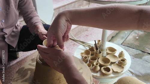Instructor guiding student's hands shaping clay vessel on a potter's wheel