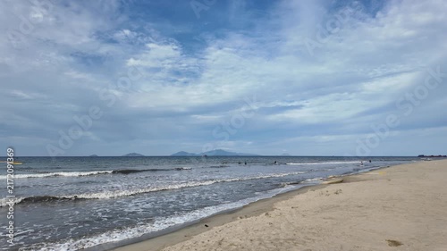 Wide view of sandy ocean beach with gentle waves under a partly cloudy sky