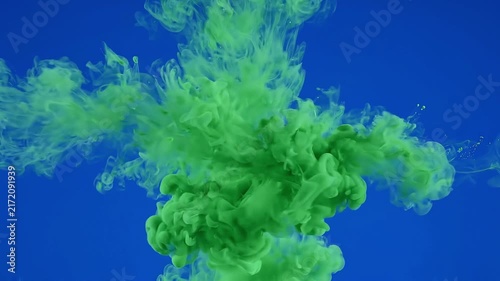Vibrant green ink expanding and dissolving gracefully in deep blue water forming artistic fluid clouds.