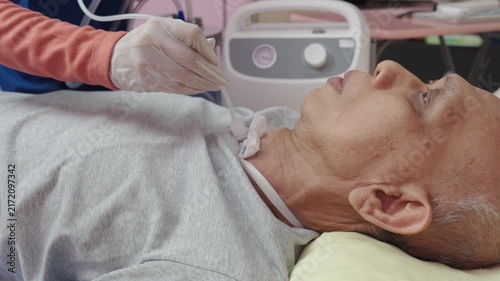 Asian nurse suctions mucus from a tube in the throat of a patient who had a tracheostomy and is recovering at home 