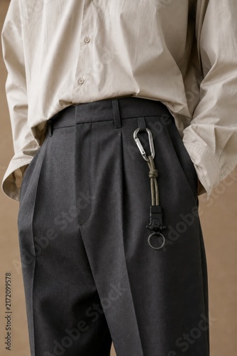 Professional individual in cream button-down shirt and dark gray wide-leg trousers accessorized with a sleek metal carabiner on belt loop, urban casual business attire, minimalist fashion statement