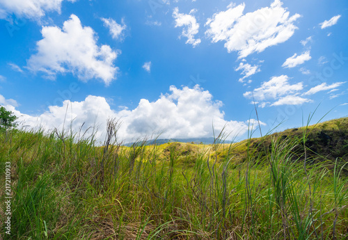 Serene rural landscape featuring lush green grass and rolling hills beneath a clear blue sky. A peaceful nature scene at the Batu Angus tourist area in Bitung, Indonesia.