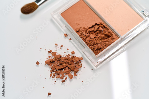 Foto Cosmetic powder spills on a white surface with a brush nearby and a compact case