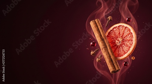 Spiced mulled wine ingredients with cinnamon stick, dried grapefruit slice and clove in red steam, cozy winter hot beverage concept, dark burgundy background with copy space for banner design