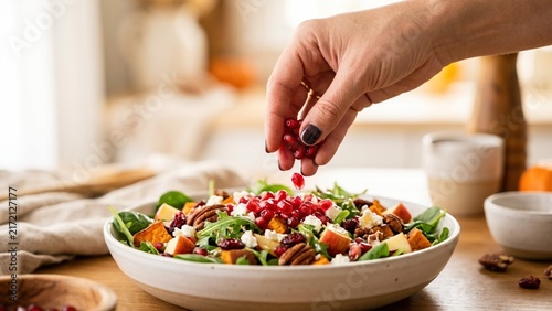 Woman Hand Adding Fresh Pomegranate Seeds To Gourmet Autumn Salad