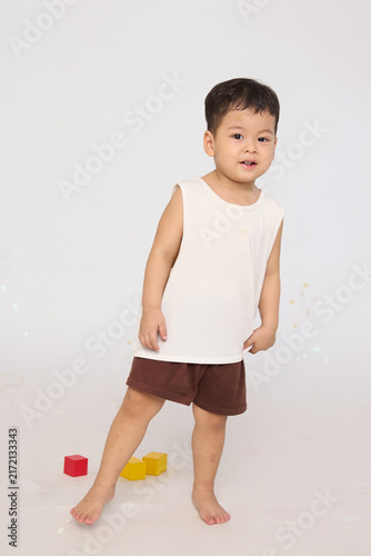 A 3-year-old toddler standing in a basic pose, wearing brown shorts and a white short-sleeved shirt.