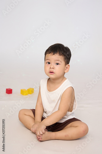 A 3-year-old toddler sitting in a basic pose, wearing brown shorts and a white short-sleeved shirt.