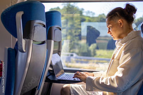 Mid adult 40s businessman working on laptop computer from train seat beside window. Concept of remote employment business travel corporate mobility and digital productivity during rail journey