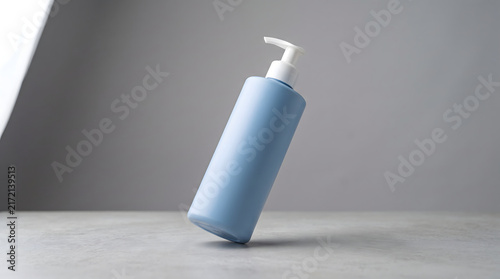 Fotografie Blue cosmetic bottle with white pump dispenser standing on a grey surface