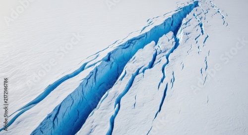 Aerial view of a deep blue crevasse splitting a vast white glacier, showing sharp ice edges and frozen textures in a cold arctic landscape representing climate change and environmental