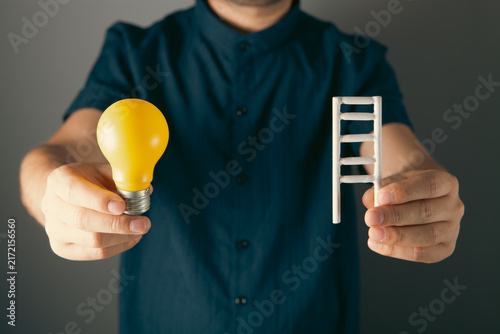 фотографія Businessman holding a light bulb and a ladder on a gray background