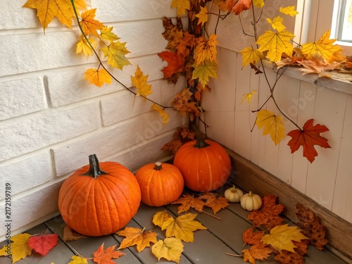 Autumn pumpkins with colorful maple leaves arranged in a cozy corner with soft light during fall harvest season