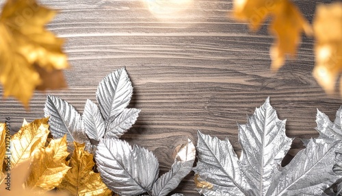 Elegant composition of gold and silver metallic autumn leaves scattered on a rustic dark wood textured background