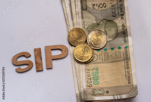Indian currency notes with coin and alongside wooden SIP blocks, systematic investment planning , budgeting, and personal finance management concept.