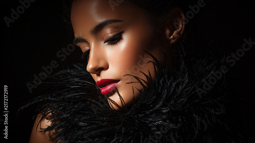 Elegant woman with makeup and black feathered accessory in dark studio lighting