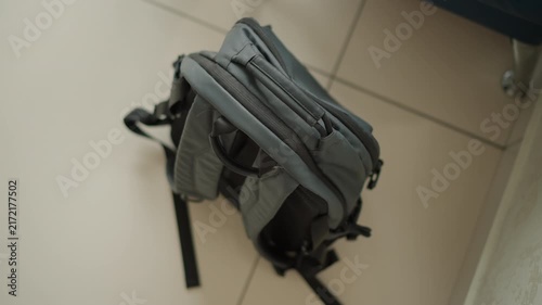Close up of gray backpack resting on light colored tiled floor with soft lighting. bag features multiple compartments zippers and adjustable shoulder straps showcasing its texture detail