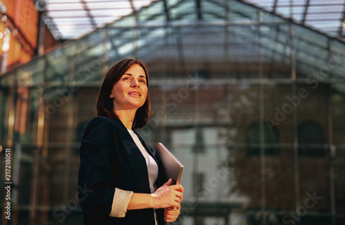 Confident businesswoman with a laptop outside a glass office building