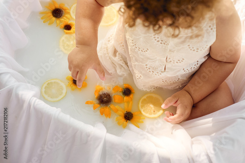     Cute curly haired toddler sitting in a white bath surrounded by lemons