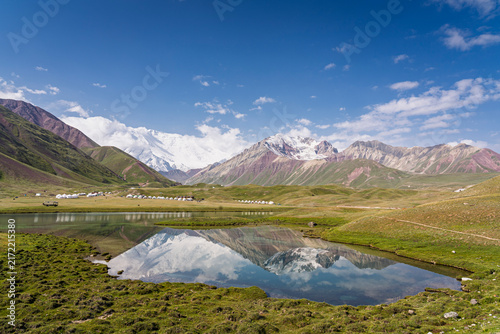 Scenic landscape view of Tulpar Kul lake and yurt camp with Lenin Peak and reflection, Trans Alay mountain range , Sary Mogul, Kyrgyzstan