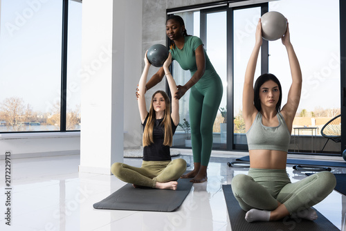 Women practicing yoga with instructor and medicine balls in a bright studio