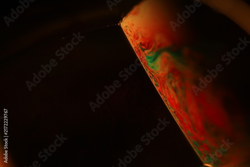 Quadro su tela Inclined liquid film facet with vibrant red and green fluid marbling in low key