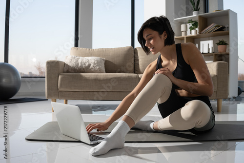 Woman doing yoga at home while following an online fitness class on her laptop